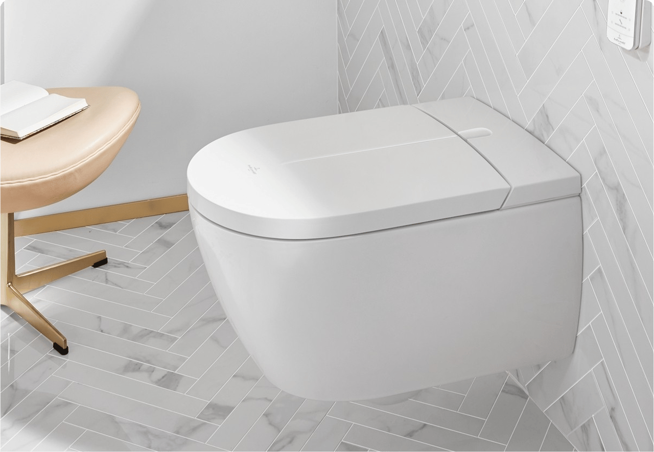 Een wit douchetoilet met wandbediening, geplaatst tegen visgraattegels op muur en vloer in marmerlook. Hoogwaardige technologie van x²o badkamers.